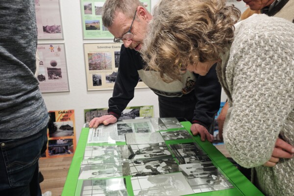 Zwei Besucher des Kulturstammtisches betrachten ausgestellte Fotografien in einer Vitrine.